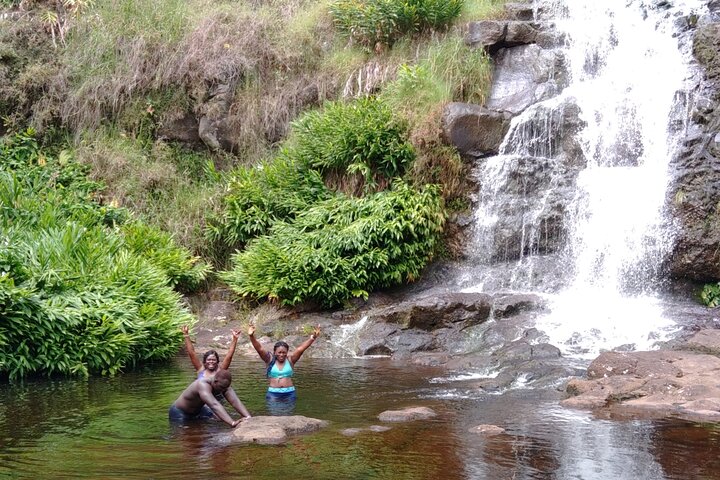 Two guests with hands raised in a private jungle waterfall pool.